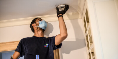 A technician working on an air quality device on the ceiling.