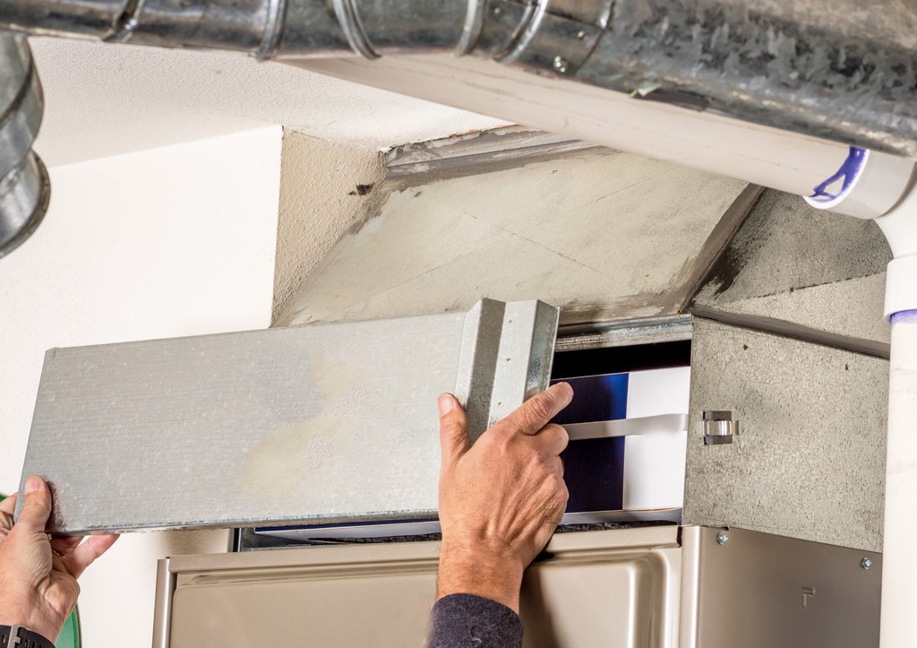 Close view of HVAC technician's hands removing the access panel on a furnace.