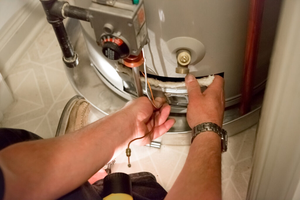 Close view of plumber's hands as they remove an access panel on a water heater.