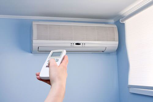 Homeowner using remote to control mini-split installed high up on light blue wall in a New York home