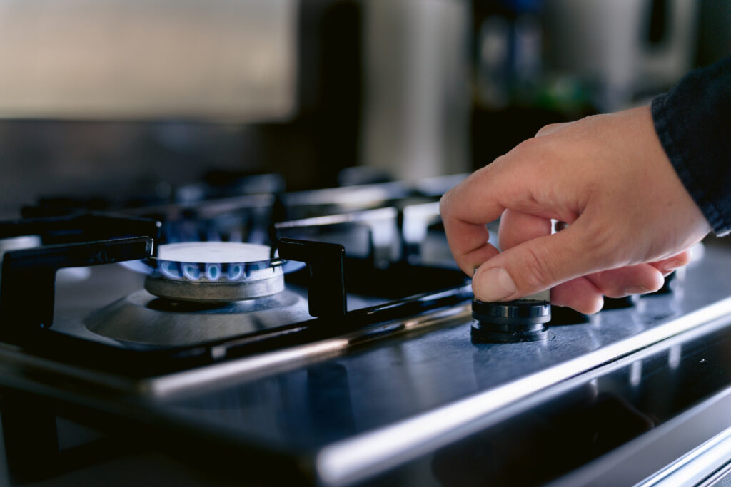 Close-up of a hand turning on a burner on a gas stove.